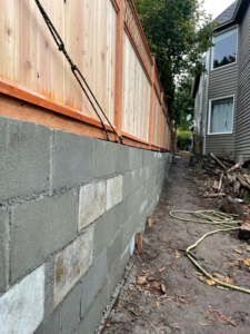 A concrete block retaining wall under construction with a new wooden fence being installed above it by A.T service in Kent, WA.