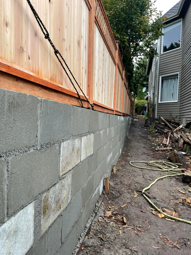 A concrete block retaining wall under construction with a new wooden fence being installed above it by A.T service in Kent, WA.