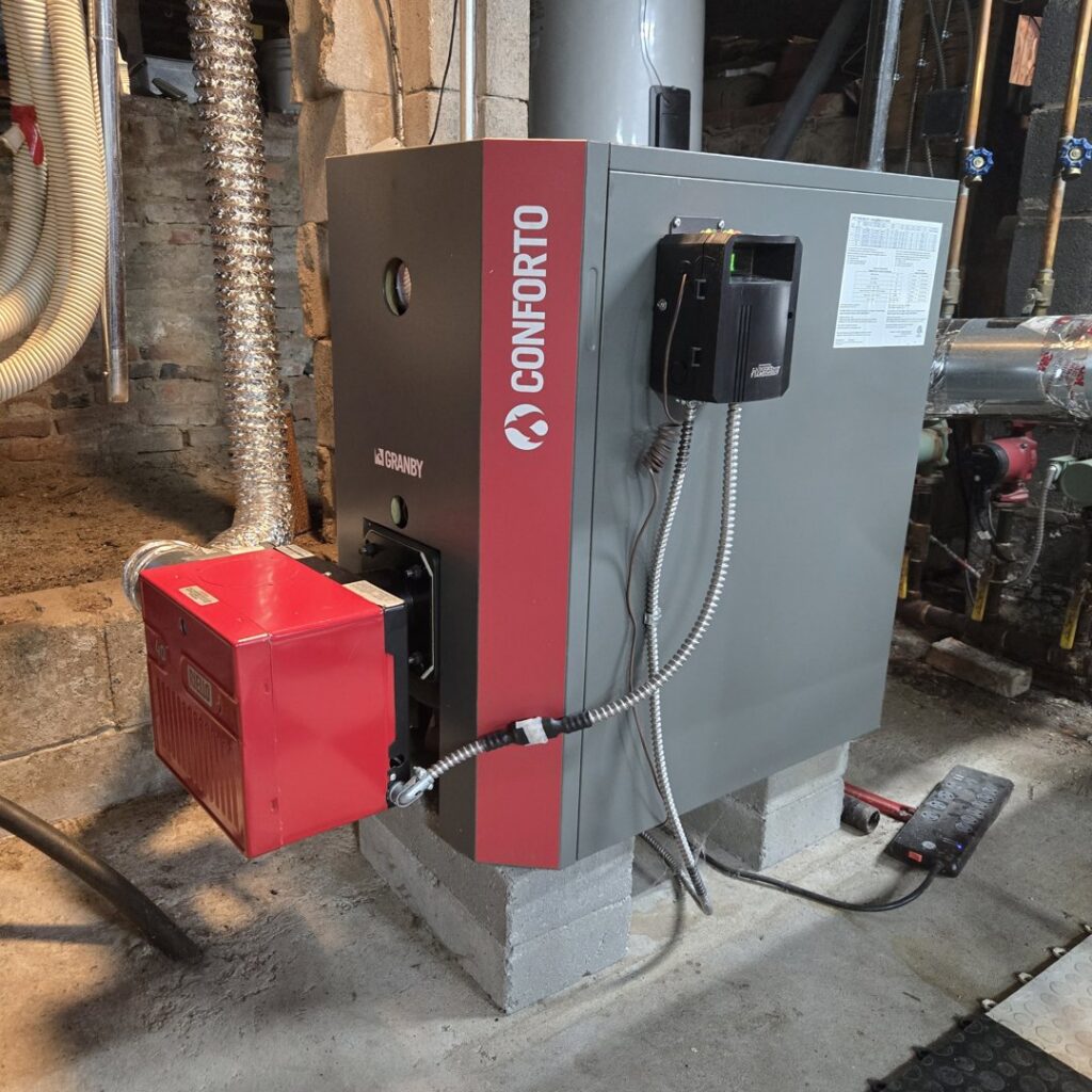 A new Conforto boiler unit with a red burner installed on concrete blocks by Advanced Comfort LLC in Concord, NH.