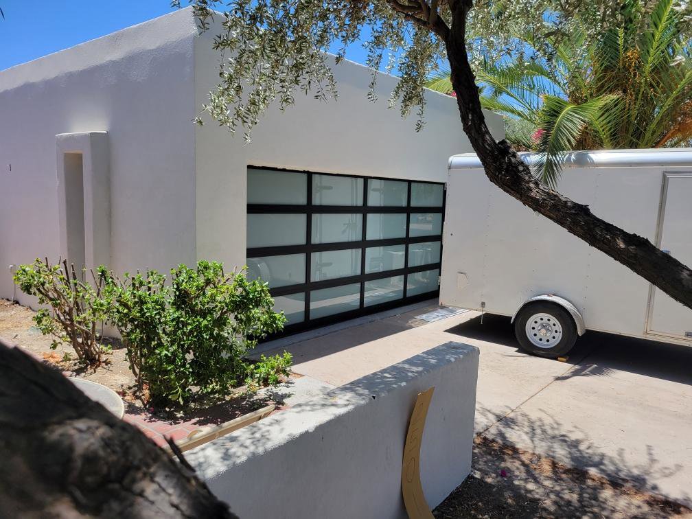 A contemporary glass garage door installed on a white building, showcasing modern design by JT's Overhead Doors in Gilbert, AZ.