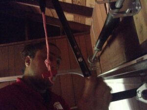 A contractor adjusting or repairing a garage door spring mechanism during a service call by OklaHome Overhead Doors in Tulsa, OK