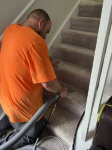 A carpet contractor from J&P United cleaning carpeted stairs with a specialized tool in Rochester, NY.