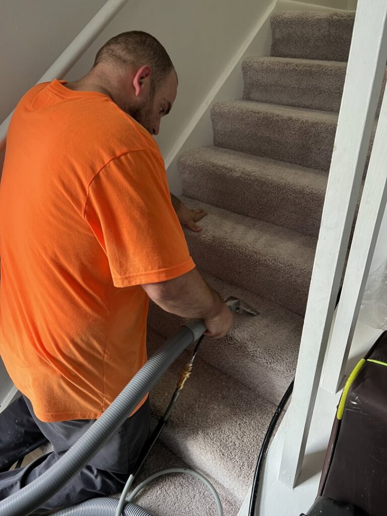 A carpet contractor from J&P United cleaning carpeted stairs with a specialized tool in Rochester, NY.