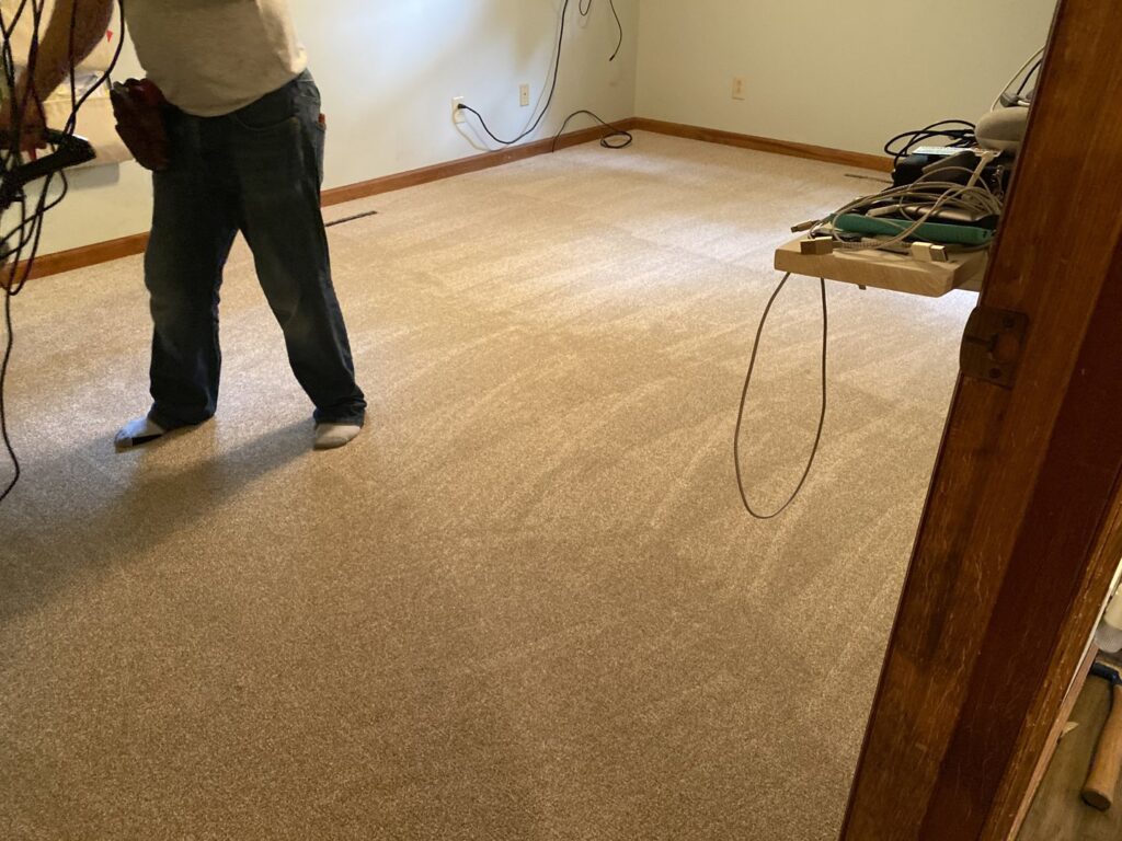 A contractor installing new beige carpet in a residential room by Hughes Floor Covering, Inc in Charlotte, NC.