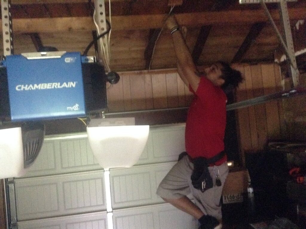 A contractor meticulously wiring a Chamberlain garage door opener during installation or repair by OklaHome Overhead Doors in Tulsa, OK