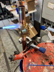 A technician soldering copper pipes during an HVAC installation, showcasing skilled work by Advanced Comfort LLC in Concord, NH.