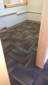 A corner of a room showcasing a precise carpet tile installation by Flooring Authority, Inc. in Amsterdam, NY.