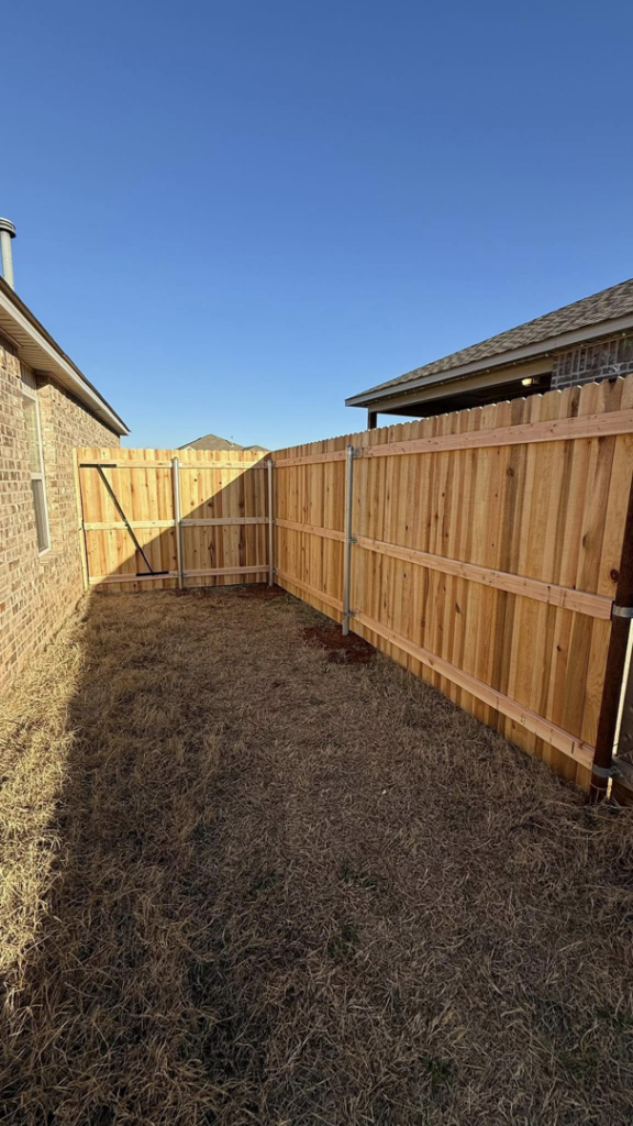 A corner of a new wooden fence with metal posts and a gate opening installed by On-Guard Fencing & Gates LLC in Oklahoma City, OK.