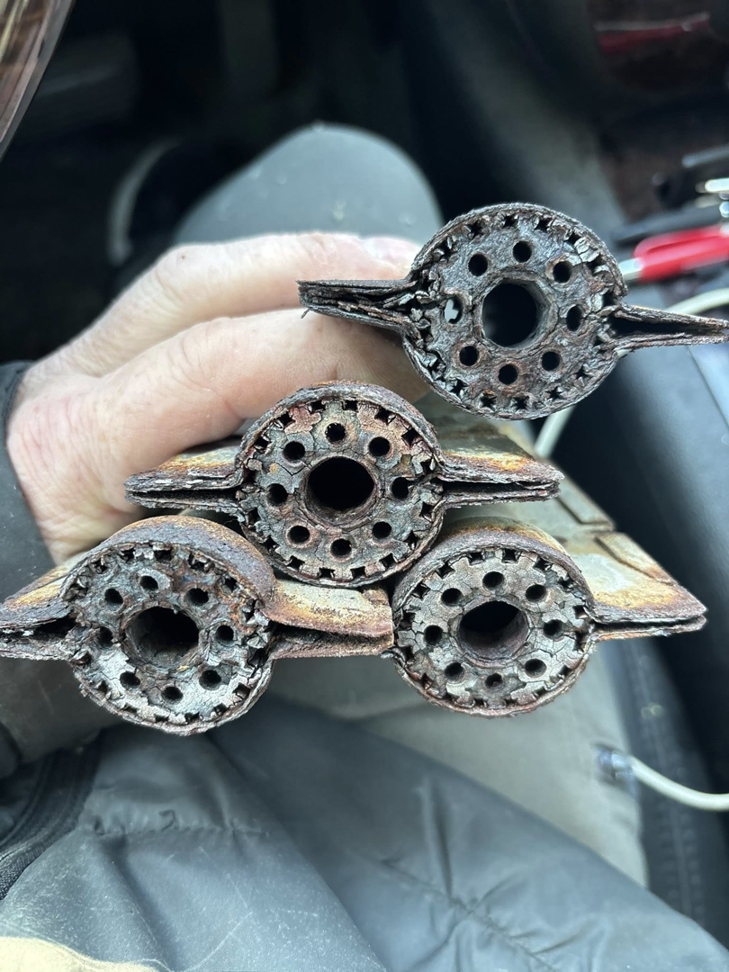 A technician holding severely corroded furnace heat exchangers, indicating a need for repair from Fine Line HVAC LLC in Isanti, MN.