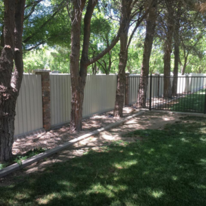A newly installed corrugated metal fence with brick pillars and a black metal gate by Pecos Construction and Fencing, LLC in Roswell, NM.