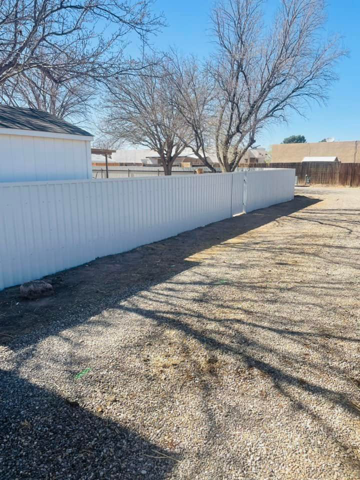 A white corrugated metal fence under construction, showing posts and panels by Pecos Construction and Fencing, LLC in Roswell, NM.
