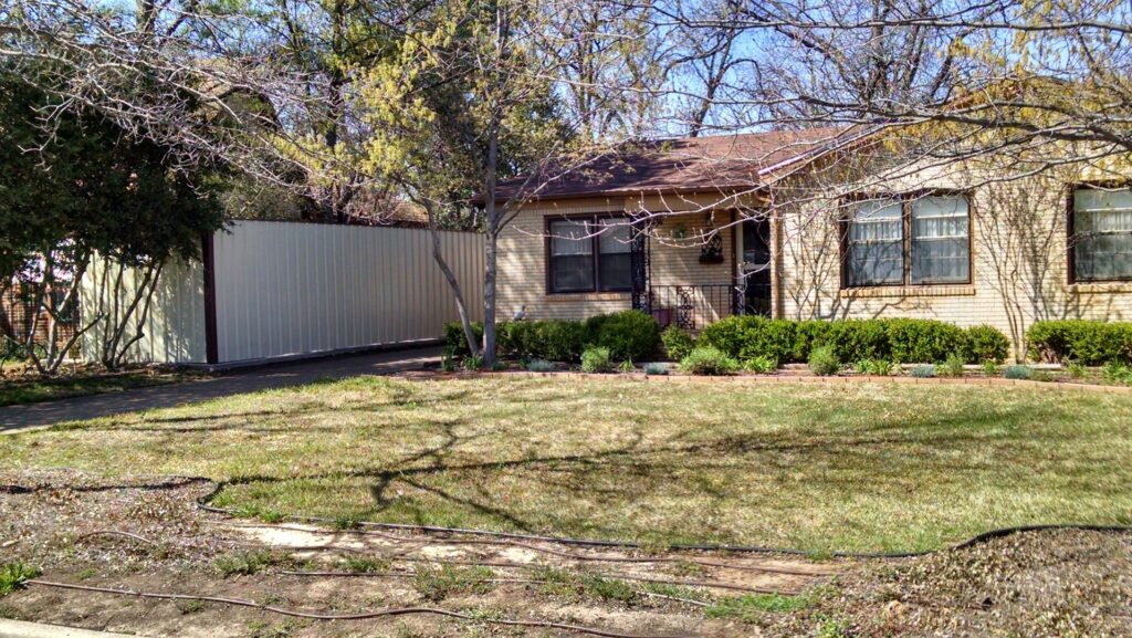 A modern corrugated metal privacy fence installed next to a residential home by Pro Insulation and Fence in Wichita Falls, TX.