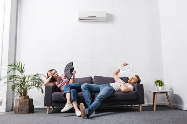 A couple relaxing under a wall-mounted air conditioning unit, highlighting cooling solutions from Joe Logan HVAC in Dayton, OH.