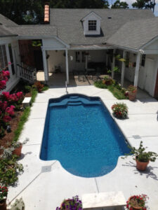 A rectangular swimming pool nestled in a charming courtyard with vibrant flowers by Central Pools, Inc. in Baton Rouge, LA