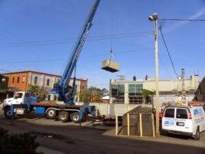 A crane installing a rooftop HVAC unit with an AireCom HVAC service van nearby in Columbus, OH.