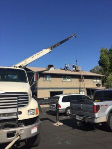 A crane installing a new HVAC unit onto the rooftop of a commercial building, with Hicken Air technicians on site in Gilbert, AZ