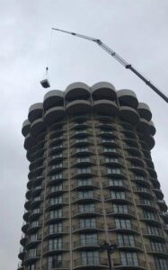 A crane lifting an air conditioning unit onto a tall building, installed by Cafco Services in Cincinnati, OH.