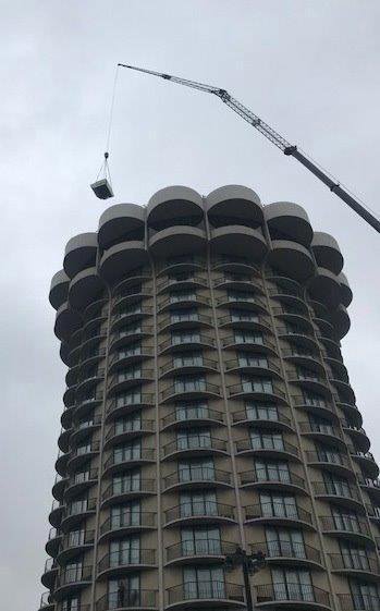 A crane lifting an air conditioning unit onto a tall building, installed by Cafco Services in Cincinnati, OH.