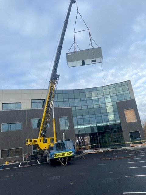 A large crane lifting a commercial HVAC unit onto the rooftop of a building, installed by ACI Northwest Heating, Cooling & Electrical in Dalton Gardens, ID.
