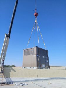 A crane lifting a large commercial HVAC unit onto a rooftop, with a worker from BH cooling & Heating in Glendale, AZ.