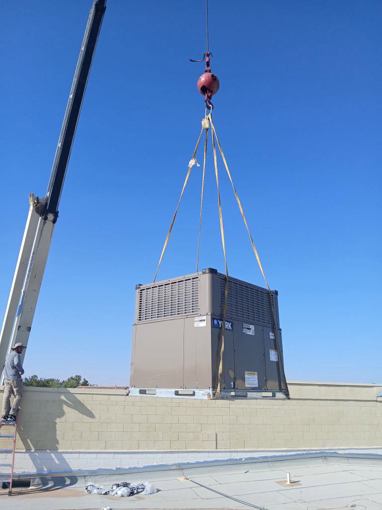 A crane lifting a large commercial HVAC unit onto a rooftop, with a worker from BH cooling & Heating in Glendale, AZ.