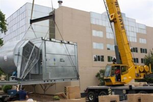 A crane lifting a large commercial HVAC unit onto a building, installed by Cafco Services in Cincinnati, OH.
