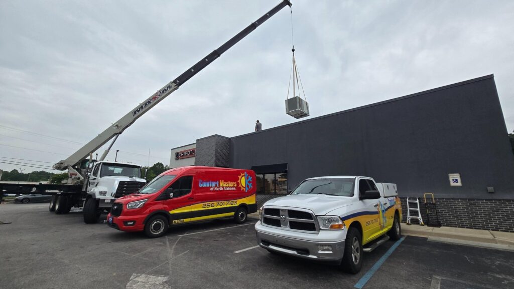 A crane lifting a new commercial HVAC unit onto a rooftop, performed by Comfort Masters of North Alabama in Athens, AL.