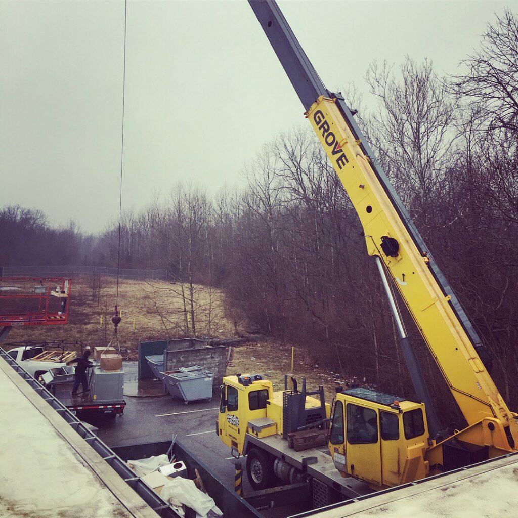 A crane lifting a large commercial HVAC unit onto a rooftop for installation by Commercial Service in Bloomington, IN.