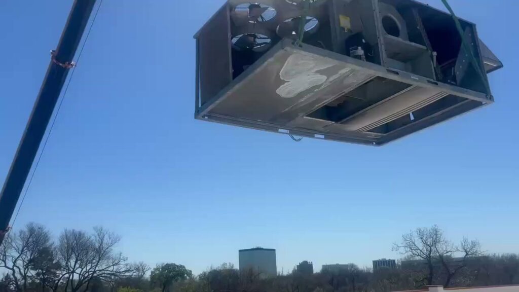 A crane lifting a large commercial HVAC unit onto a rooftop for installation by Harlen Johnson Heating & Air in Dallas, TX.