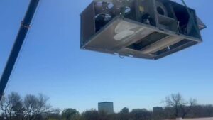 A crane lifting a large commercial HVAC unit onto a rooftop for installation by Harlen Johnson Heating & Air in Dallas, TX.