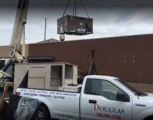 A crane lifting a large commercial York HVAC unit onto a rooftop, indicating installation by Douglas Cooling & Heating in Pelham, AL.