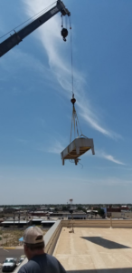 A crane lifting a large commercial HVAC unit onto a rooftop for installation by Klimate Concepts in Lubbock, TX.