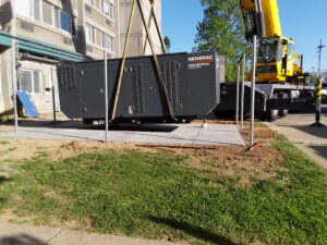 A crane lifting a large Generac industrial power generator into place for installation by Varitech, Inc. in Louisville, KY.