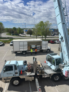 A crane lifting large HVAC equipment from a truck during a commercial installation project by Omaha Heating and Air in Omaha, NE.