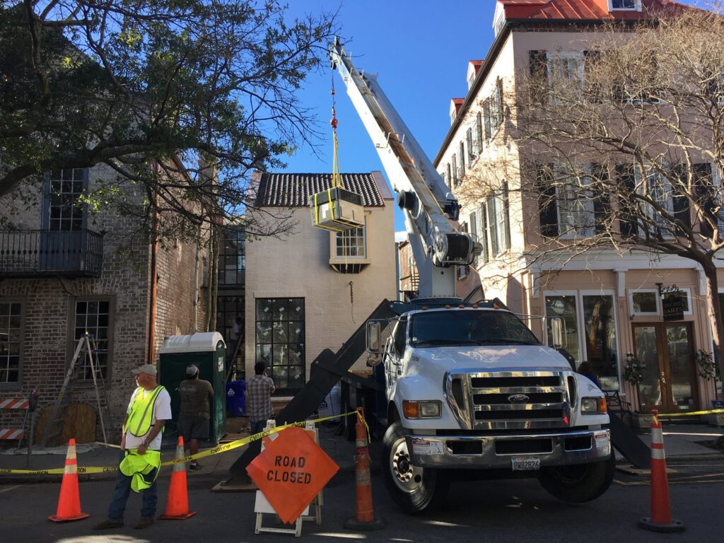 A crane lifting an HVAC unit during an installation in a city street by AC Heating and Air Conditioning Services in Charleston, SC.