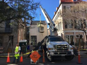 A crane lifting an HVAC unit during an installation in a city street by AC Heating and Air Conditioning Services in Charleston, SC.