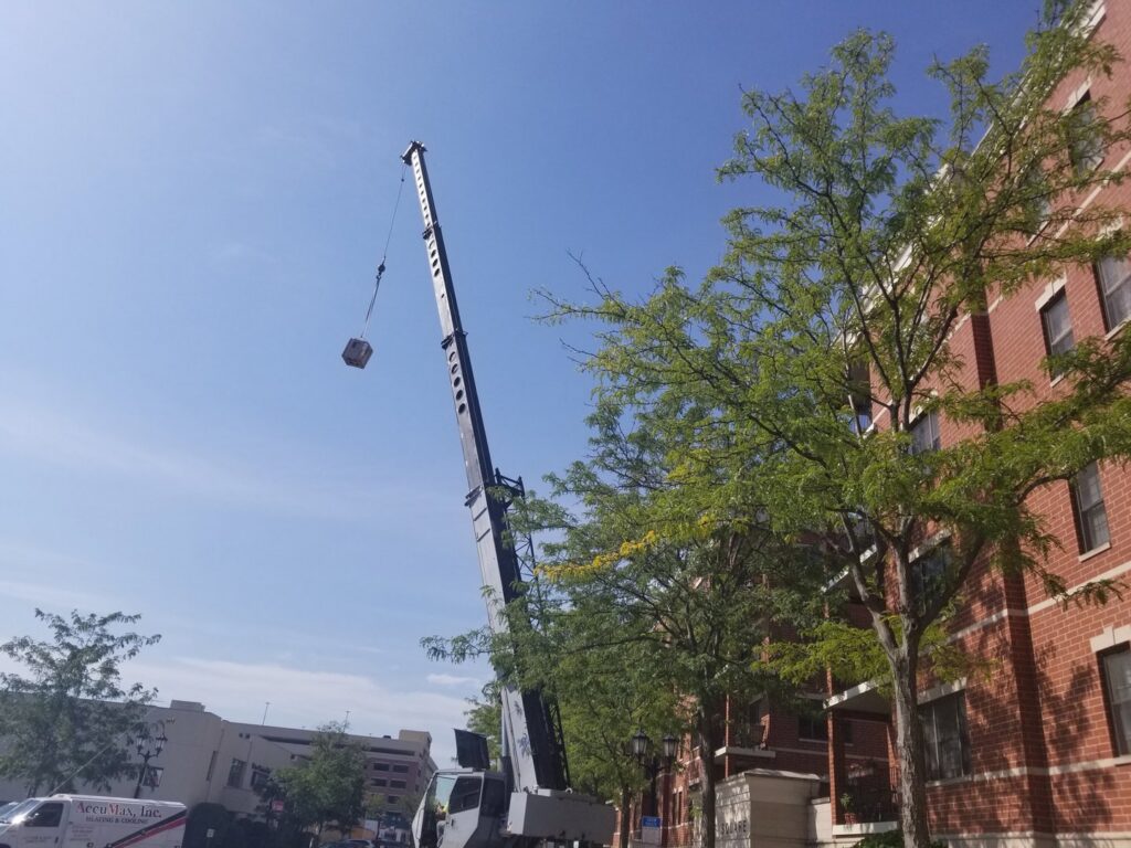 A crane lifting an HVAC unit for installation on a commercial building by AccuMax Incorporated in Aurora, IL.
