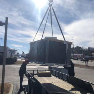A crane lifting a large commercial HVAC unit from a trailer, preparing for installation by Eleven Heating and Cooling in Birmingham, AL.