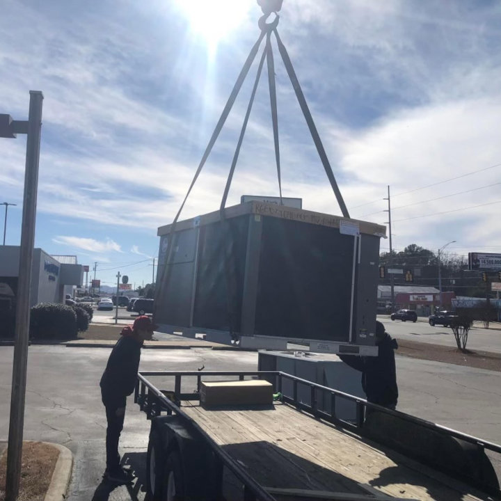 A crane lifting a large commercial HVAC unit from a trailer, preparing for installation by Eleven Heating and Cooling in Birmingham, AL.