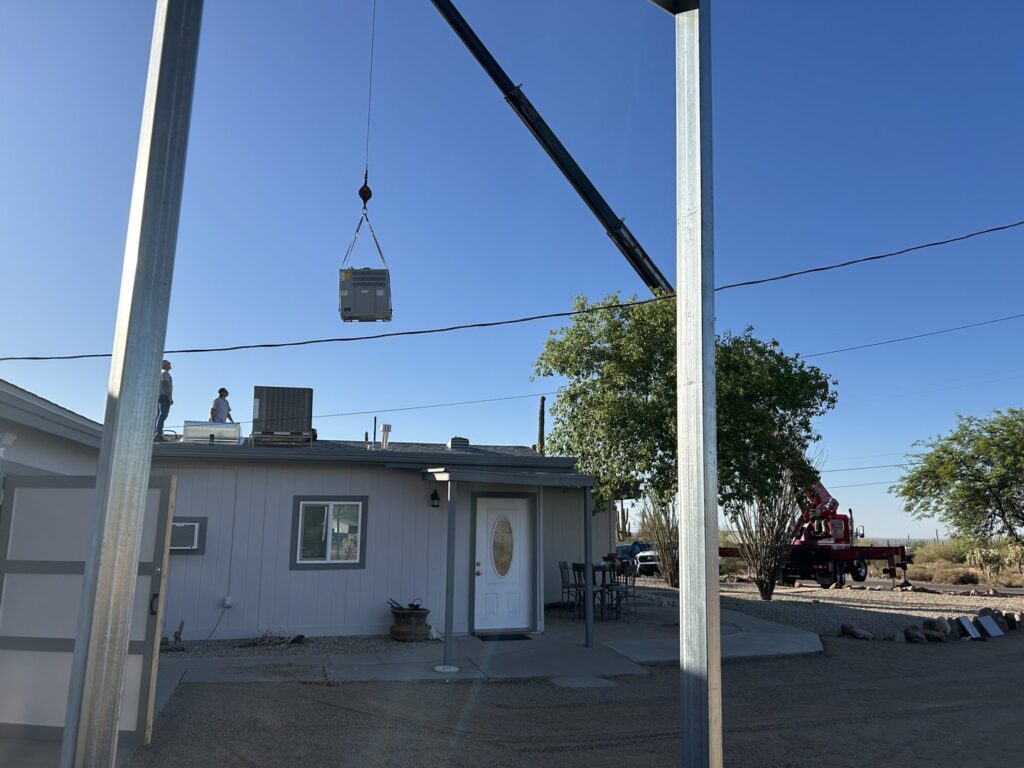 A crane lifting a new HVAC unit onto a residential roof for installation by Ash Cooling & Heating in Mesa, AZ.