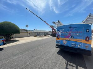 A crane lifting an HVAC unit onto a residential roof, with an AZ Perfect Comfort service truck nearby in Phoenix, AZ.