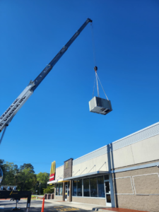 A crane lifting a new HVAC unit onto the roof of a commercial building by Facility Doctors in Raleigh, NC