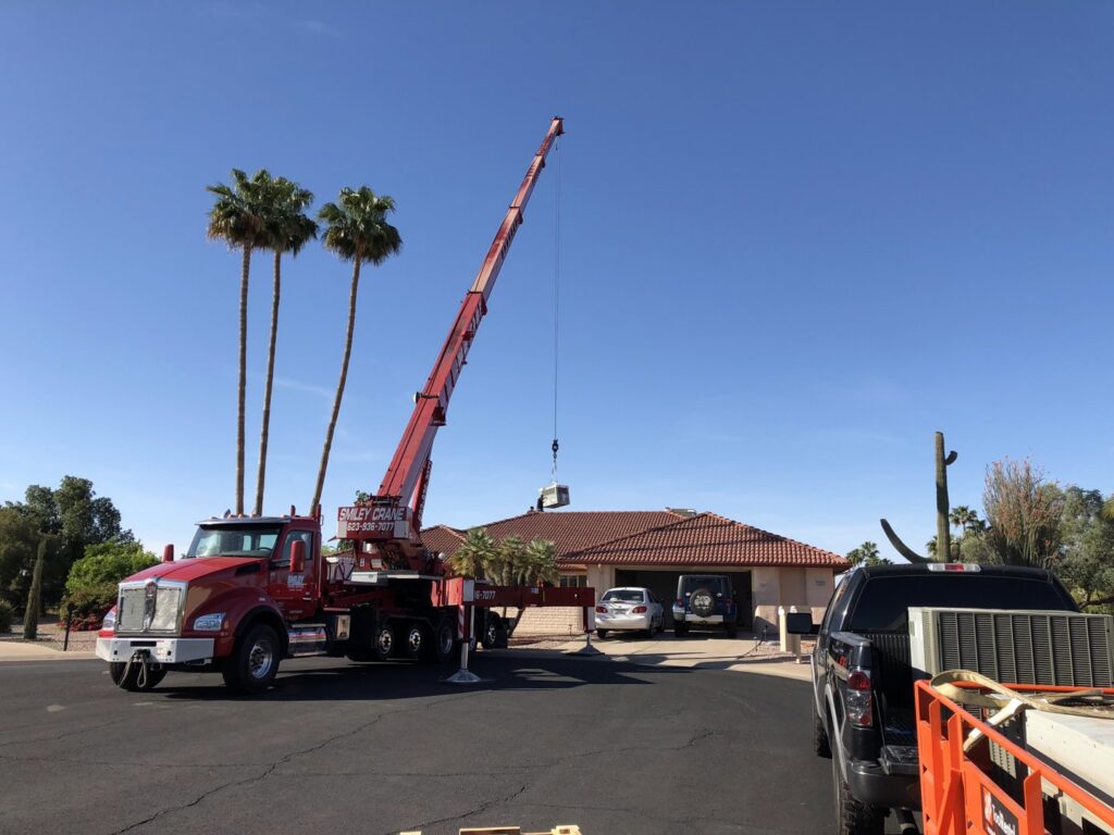A crane lifting an HVAC unit over a residential home for installation by Hellerud Air in Peoria, AZ.