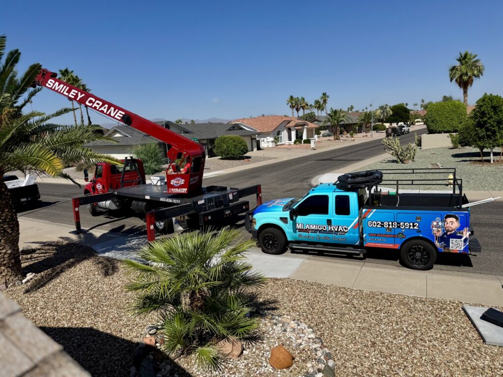 A crane lifting an HVAC unit onto a roof with a Mi Amigo HVAC service truck nearby in Surprise, AZ