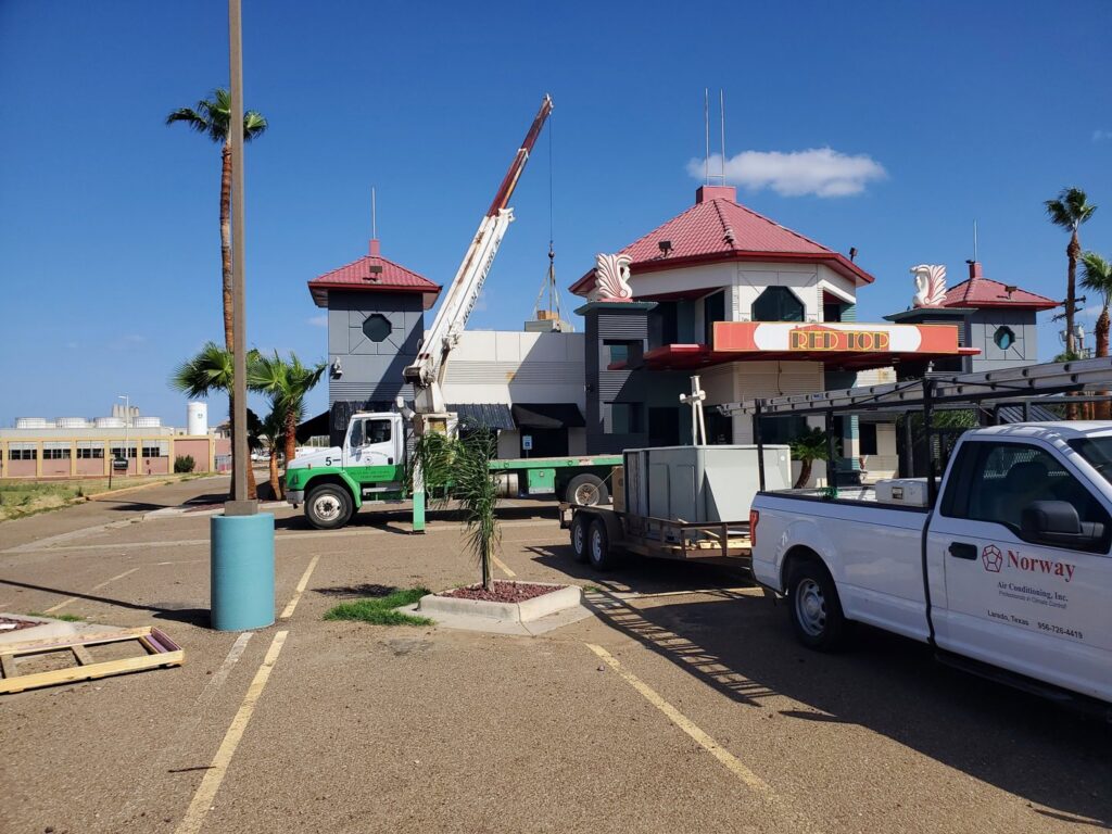 A crane lifting an HVAC unit onto a commercial building roof by Norway Air Conditioning Inc. in Laredo, TX.
