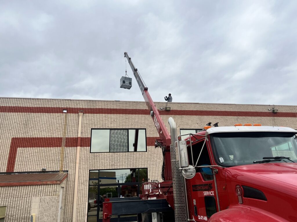 A crane lifting a new HVAC unit onto a commercial rooftop for installation by MB Heating and Air in Northridge, CA.