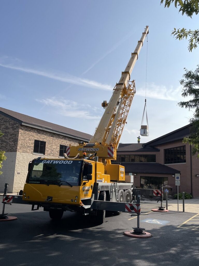 A large crane lifting an HVAC unit onto a commercial rooftop, performed by Nortek Environmental, Inc. in Naperville, IL.