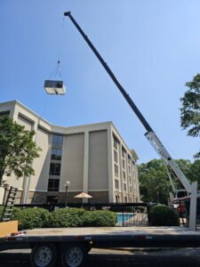 A crane lifting an HVAC unit over a building for installation by Peak Seasons HVAC in Raleigh, NC.