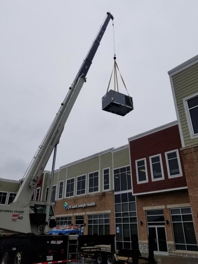 A crane lifting an HVAC unit over a commercial building for Southern Comfort Heating & Cooling in Lexington, KY