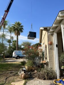 A crane lifting an HVAC unit over a residential house for installation or replacement by Hicken Air in Gilbert, AZ